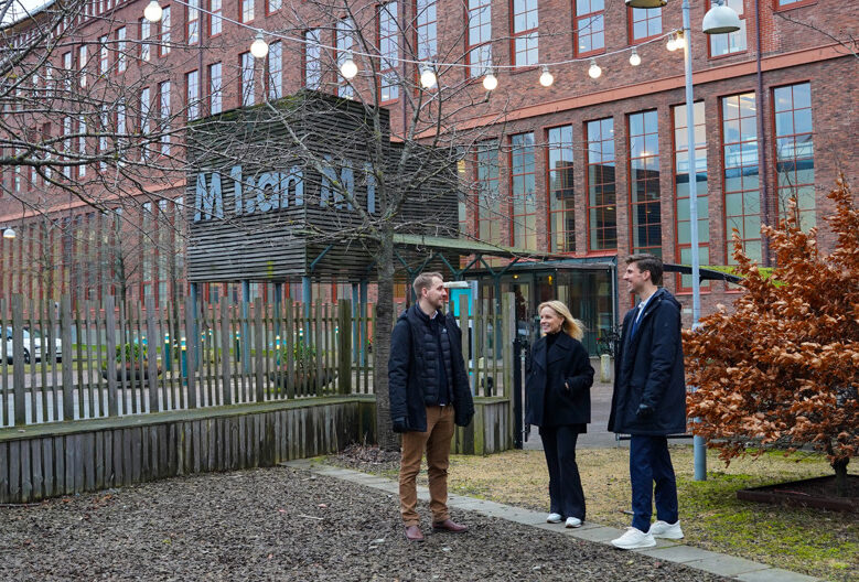Tre medarbetare står utomhus utanför fastigheten M1:an och pratar, glada.
